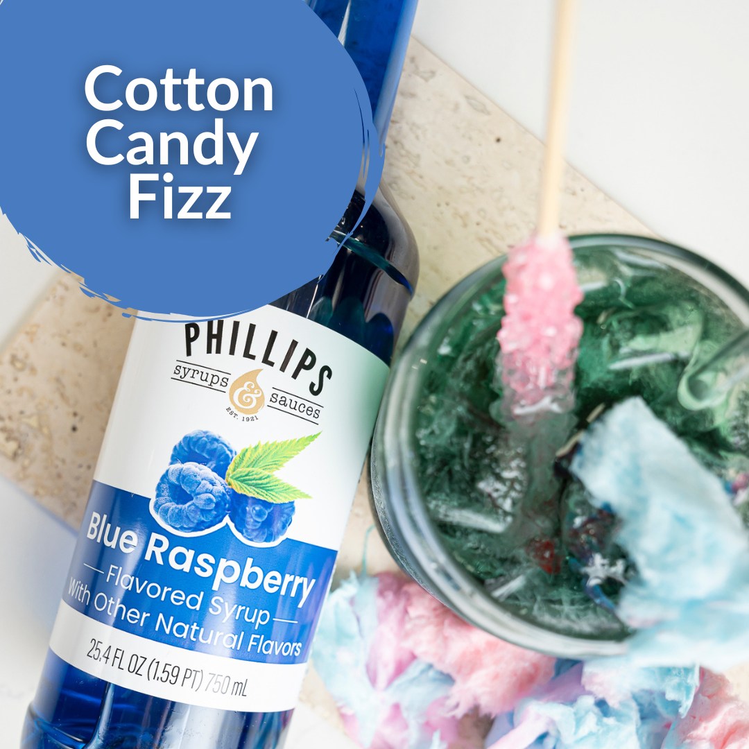 A bottle of Phillips Syrup & Sauces Blue Raspberry flavored syrup is shown diagonally next to a glass jar filled with green candy and pink/blue cotton candy, with a blue circular graphic reading 'Cotton Candy Fizz'.