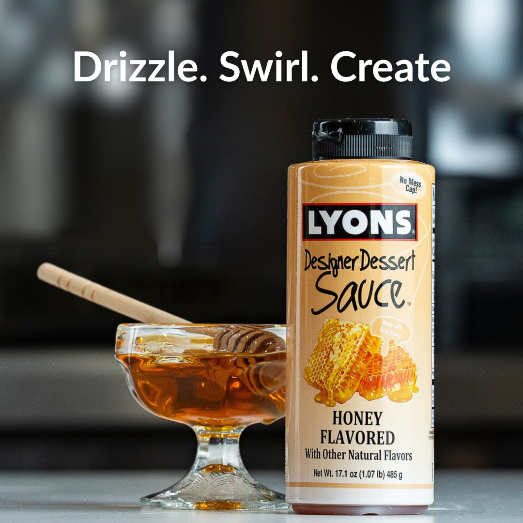 A bottle of Lyons Designer Dessert Sauce, Honey Flavored, standing next to a glass bowl of honey with a wooden dipper. The background is a dark, blurred kitchen setting with the text 'Drizzle.