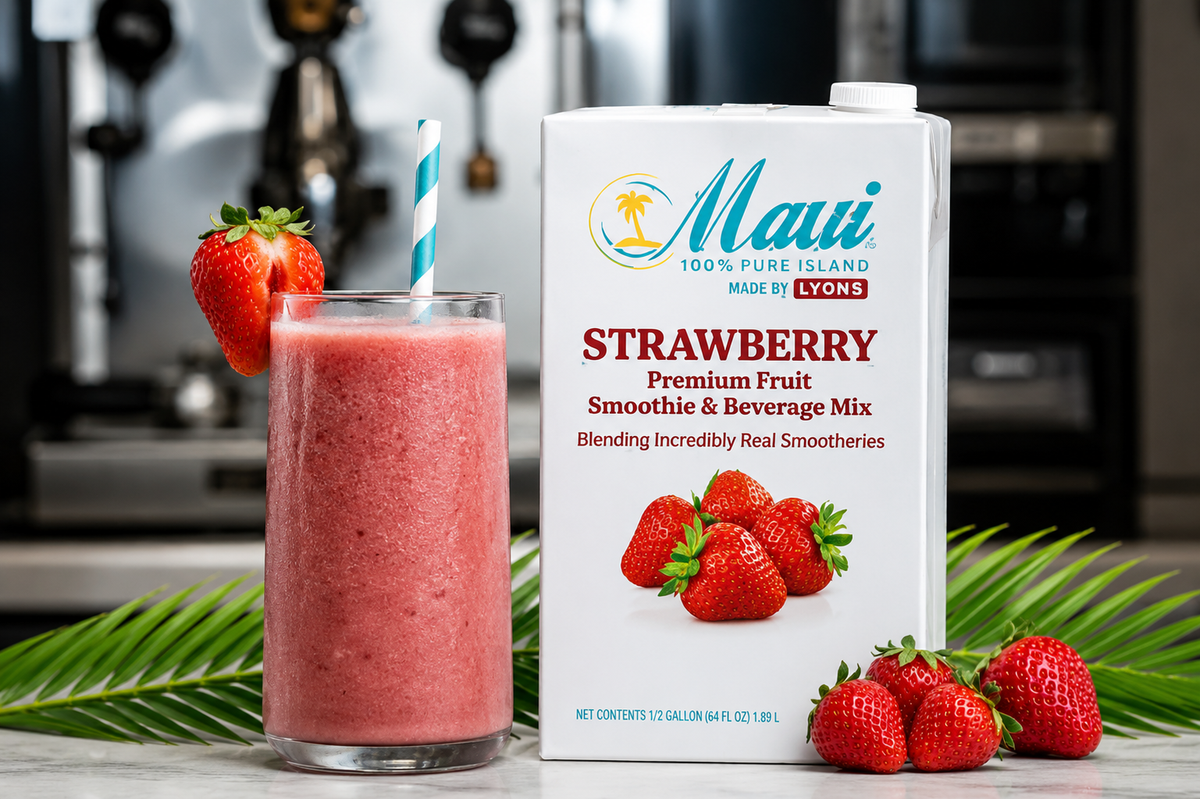 A carton of Maui 100% Pure Island Strawberry Premium Fruit Smoothie & Beverage Mix stands next to a tall glass filled with pink strawberry smoothie and a blue-and-white striped straw. Fresh strawberries and green palm leaves are arranged around the product in a kitchen setting with a blurred coffee machine in the background.