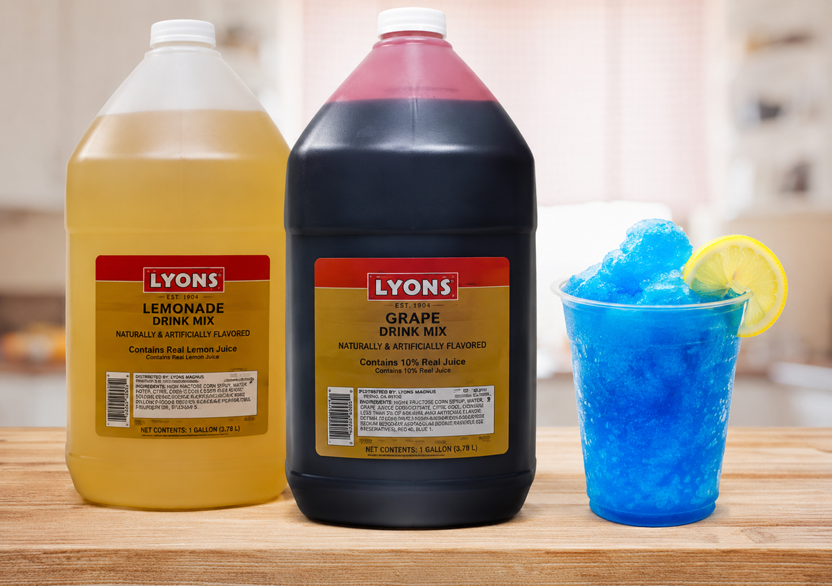 Two large bottles of Lyons Lemonade Drink Mix and Grape Drink Mix on a wooden counter next to a blue slushie cup with a lemon wedge, with a blurred kitchen background.